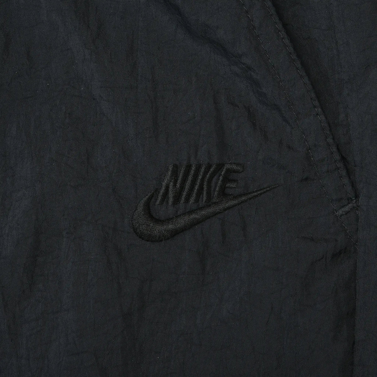 Close-up of tonal black Nike Swoosh embroidery on track pants