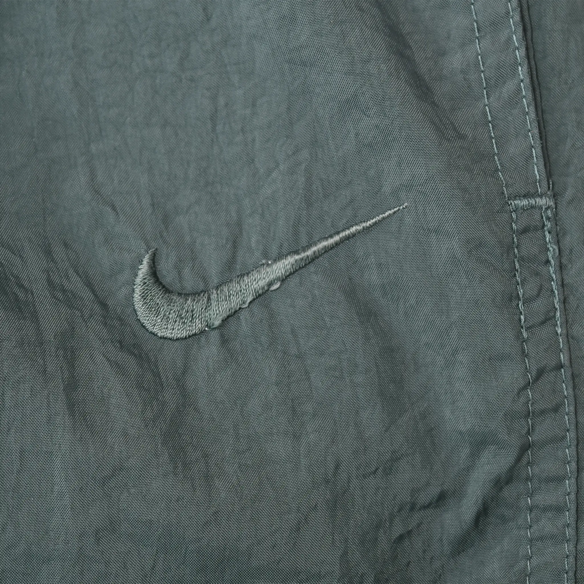 Close-up of tonal Nike Swoosh embroidery on dark green track pants