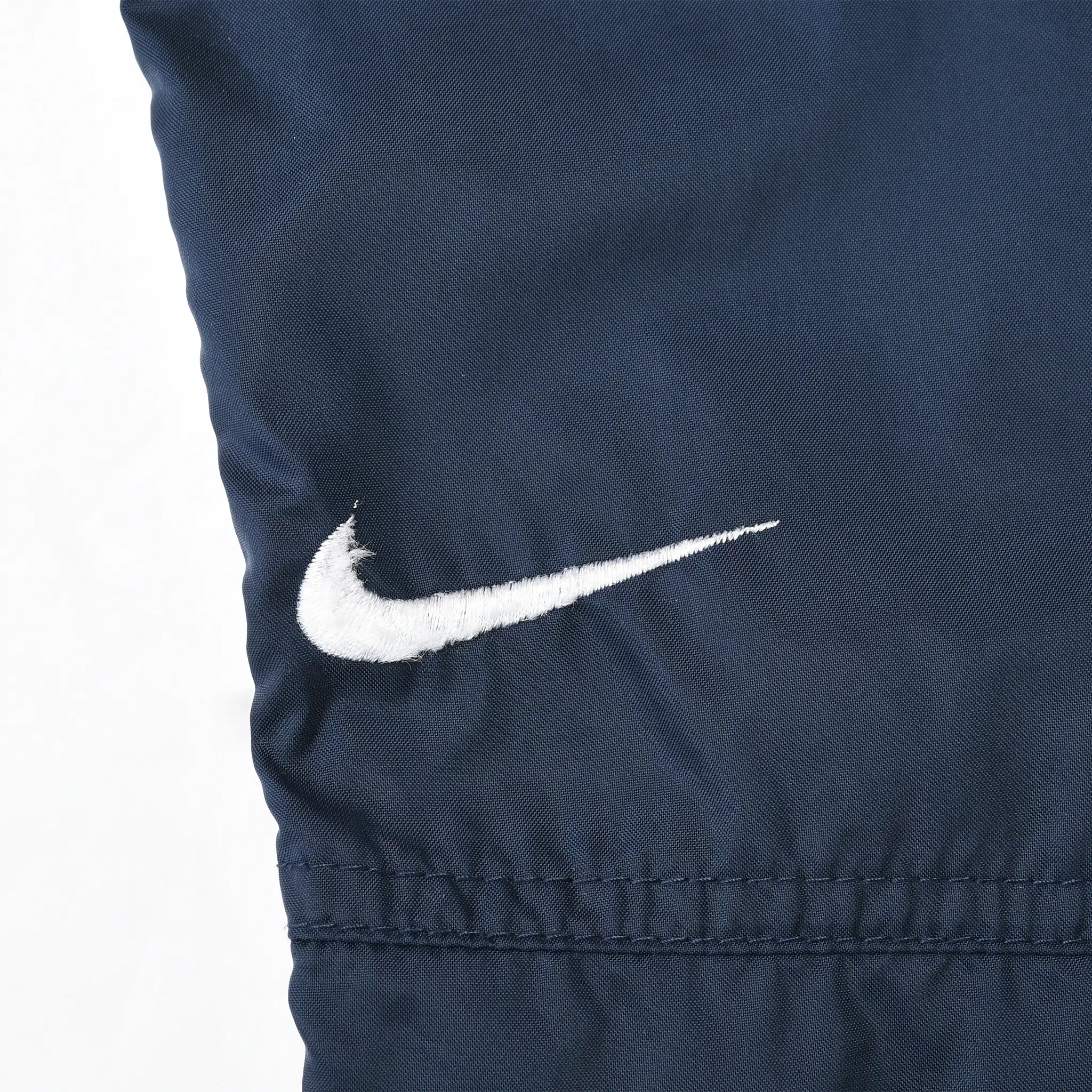 Close-up of white Nike Swoosh embroidery on navy blue track pants