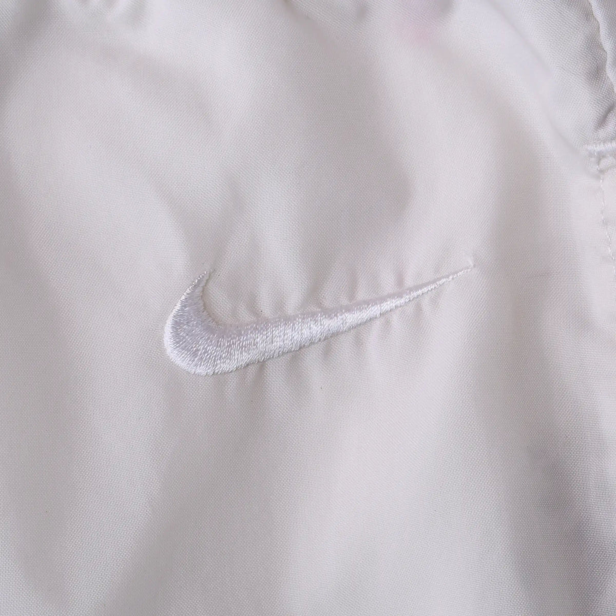 Close-up of white Nike Swoosh embroidery on white track pants