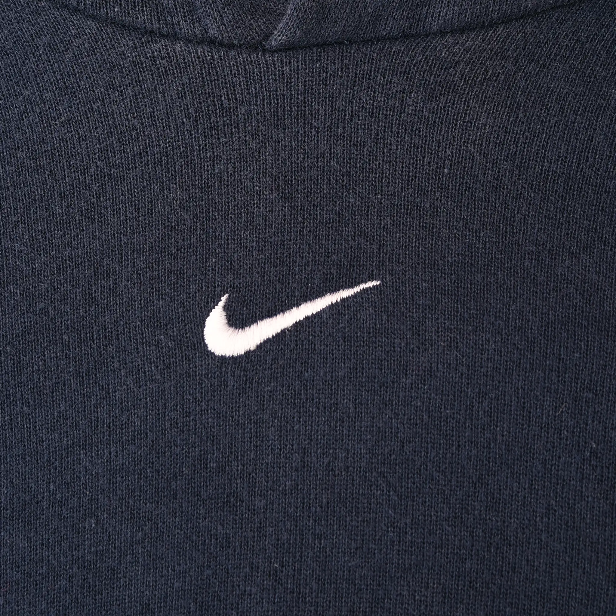 Close-up of white Nike Swoosh embroidery centered on navy blue hoodie chest
