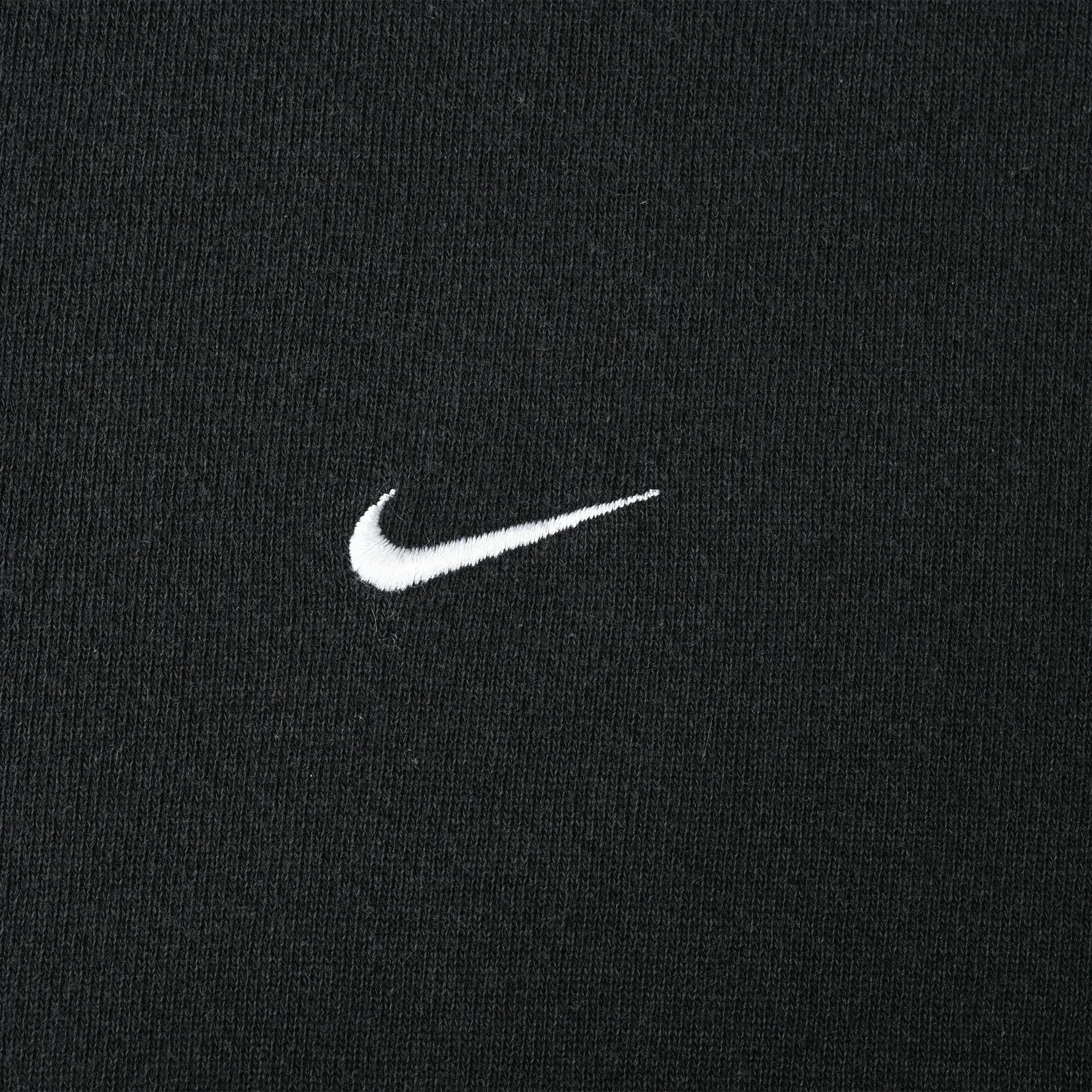 Close-up of small white Nike Swoosh embroidery on black fabric