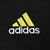 Close-up of yellow adidas emblem and white embroidered wordmark on black fleece