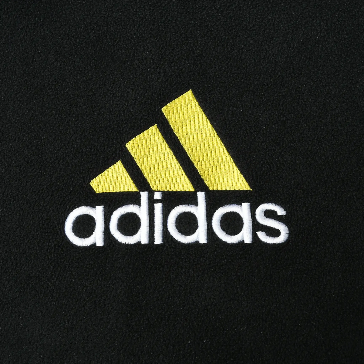 Close-up of yellow adidas emblem and white embroidered wordmark on black fleece