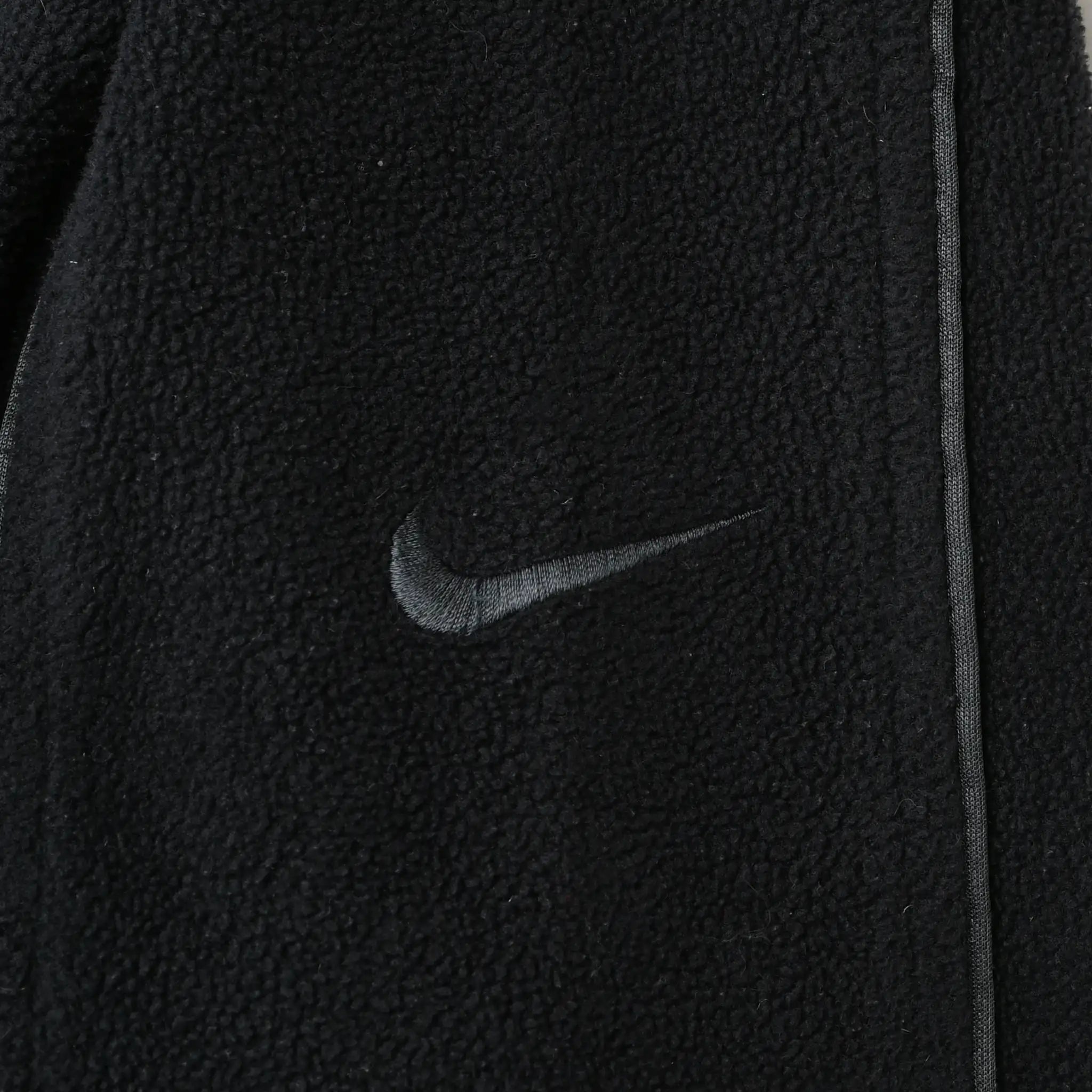 Close-up of black Nike Swoosh embroidery beside seam piping