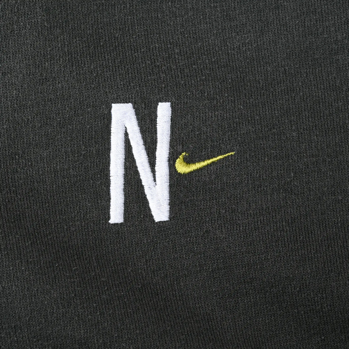 Close-up of white N and lime Nike Swoosh embroidery on dark green chest