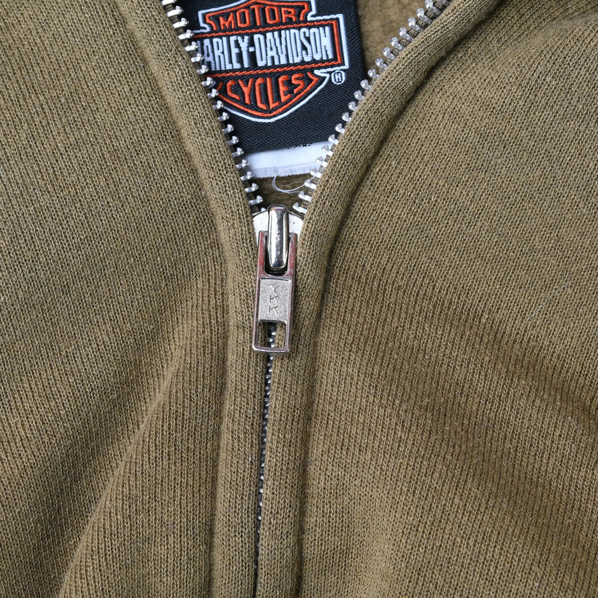 Close-up of metal zipper, khaki green fabric, and Harley-Davidson neck label