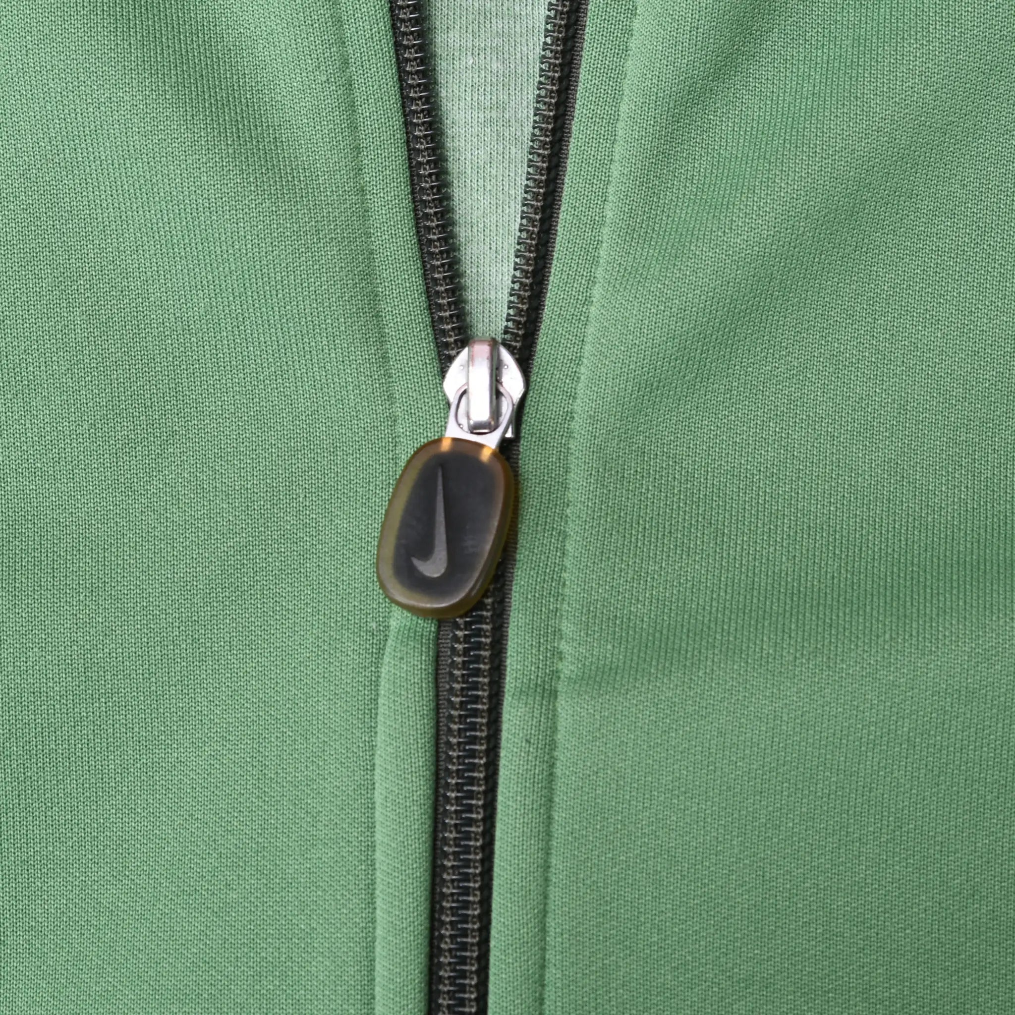 Close-up of black front zipper and oval pull on green Nike track jacket
