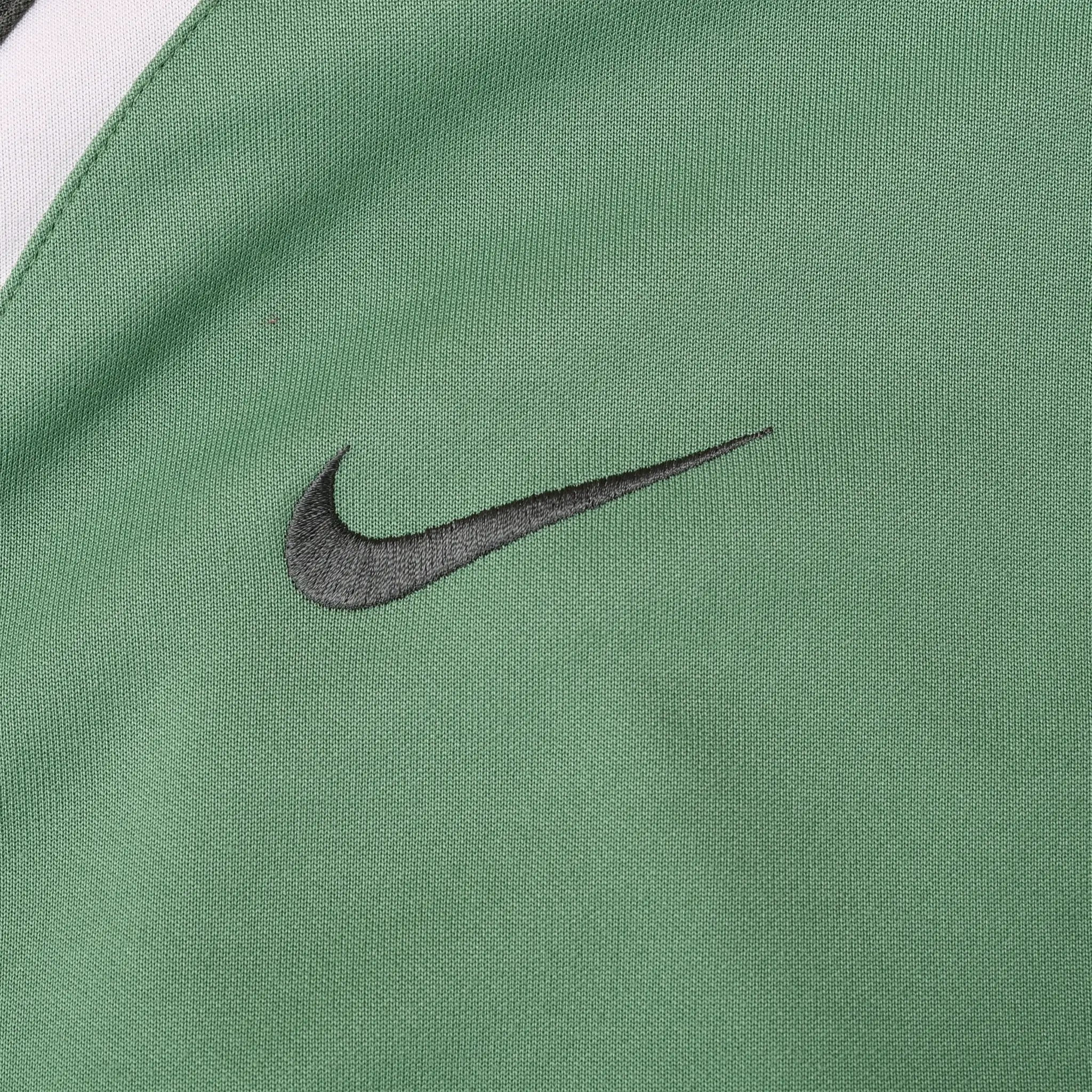 Close-up of dark gray embroidered Nike Swoosh on green jacket chest