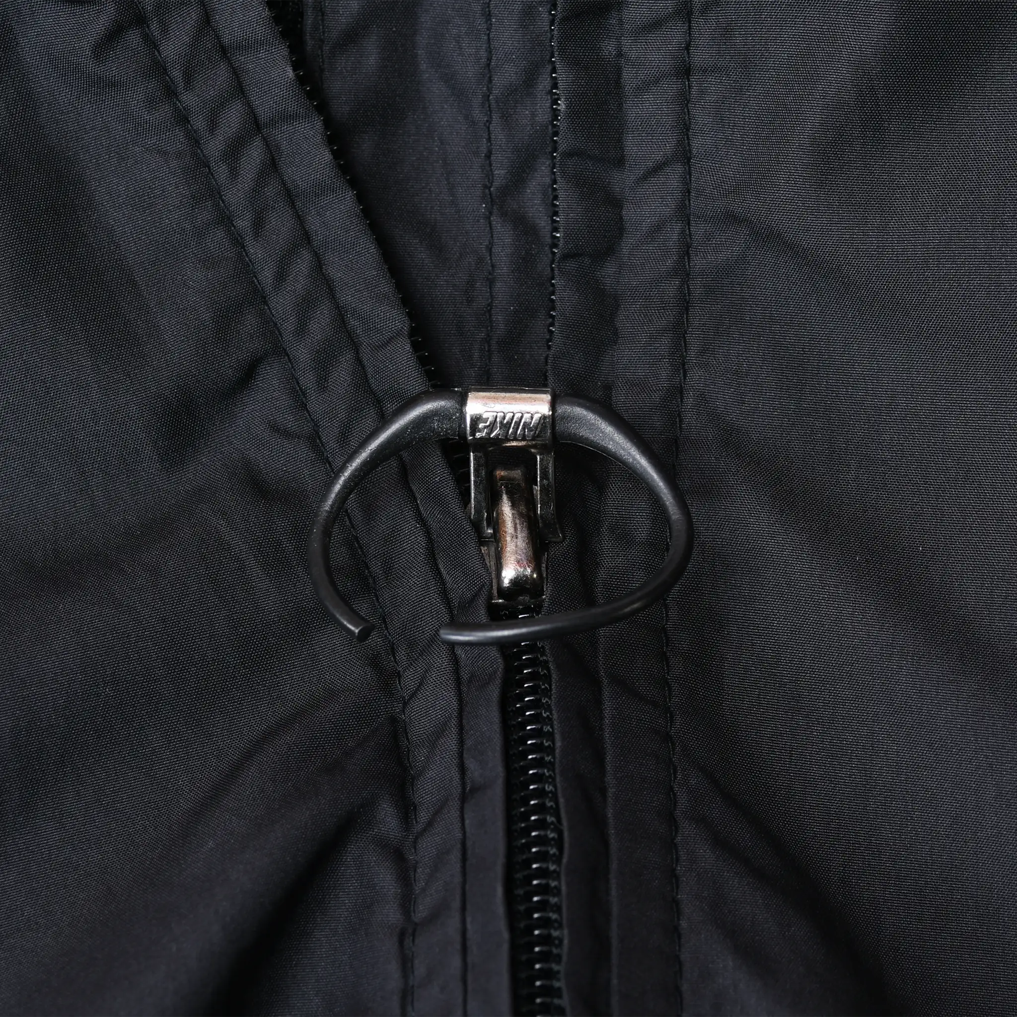 Close-up of the Nike jacket's black front zipper pull with oval cord loop