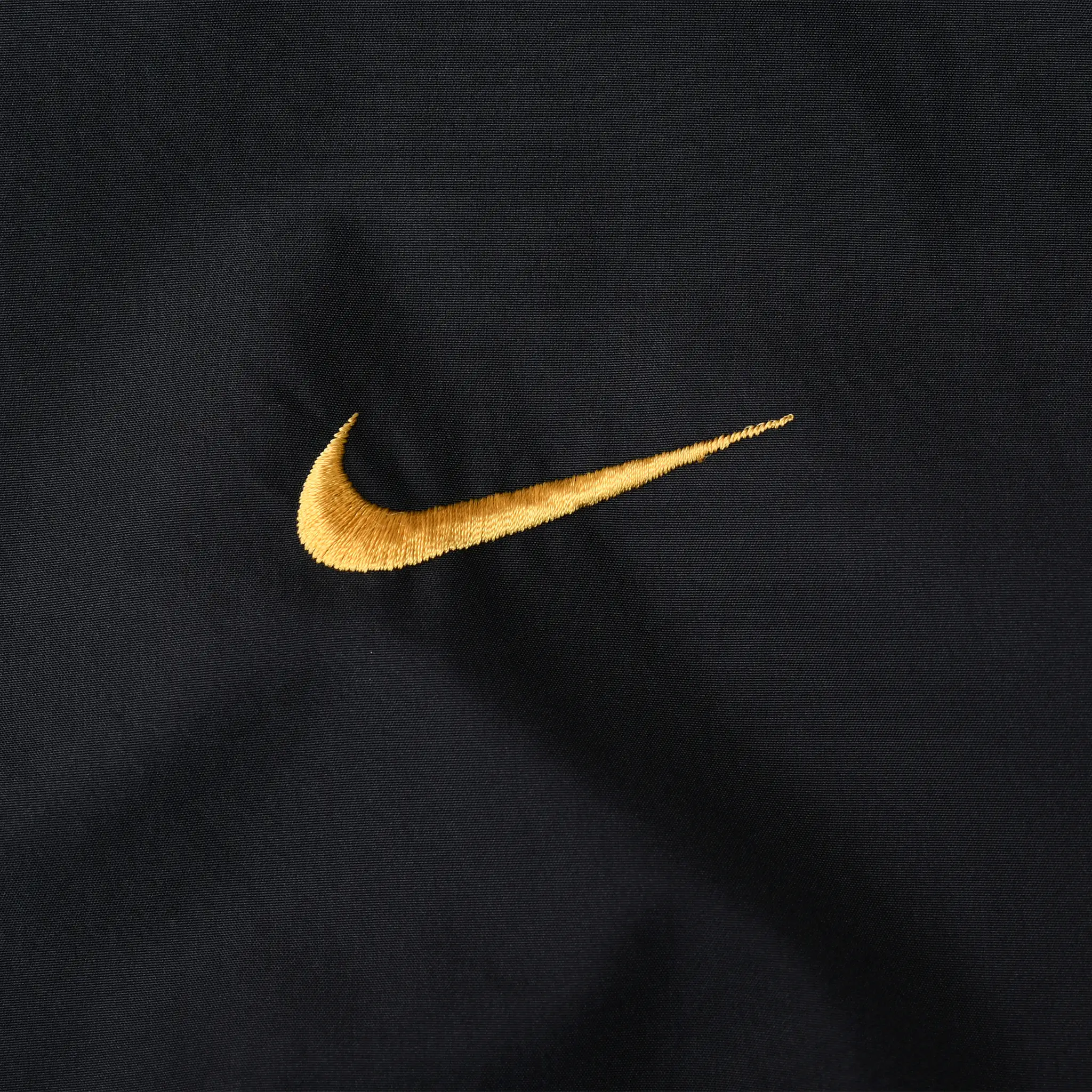 Close-up of yellow Nike Swoosh embroidery on black jacket fabric