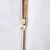 Close-up of gold front zipper and G-shaped pull against white jacket fabric
