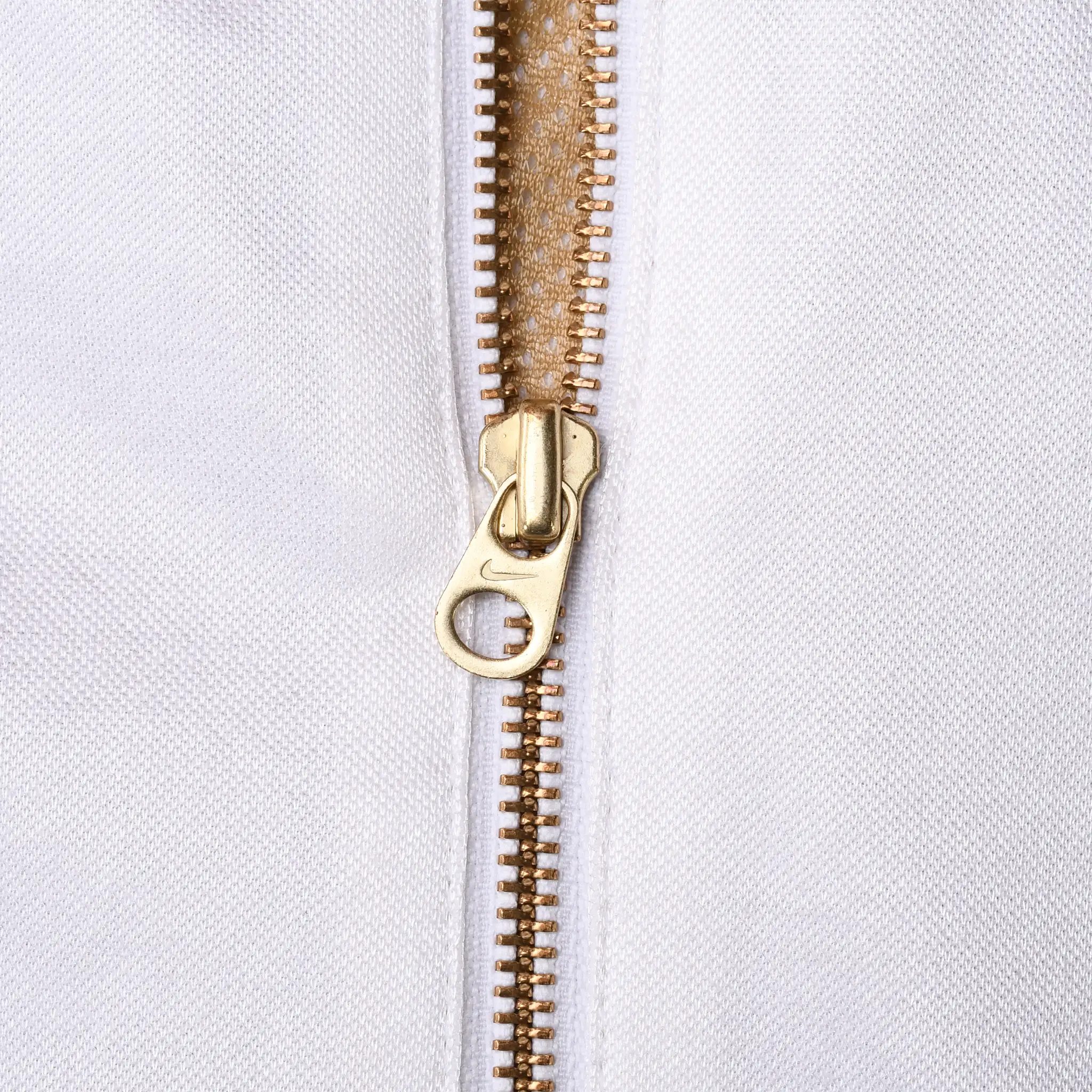 Close-up of gold front zipper and G-shaped pull against white jacket fabric