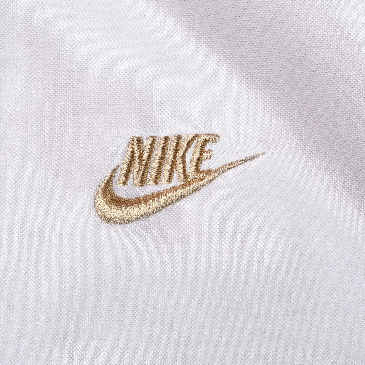 Close-up of gold Nike logo embroidery on white jacket fabric