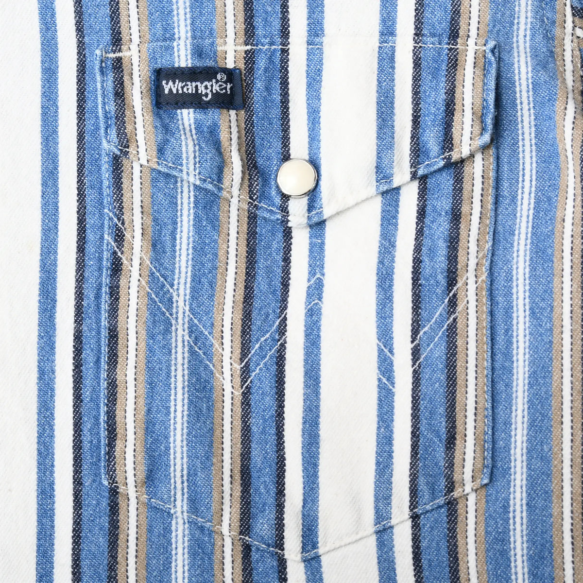 Close-up of striped chest pockets, white pearl snap, pointed flaps, and Wrangler tab