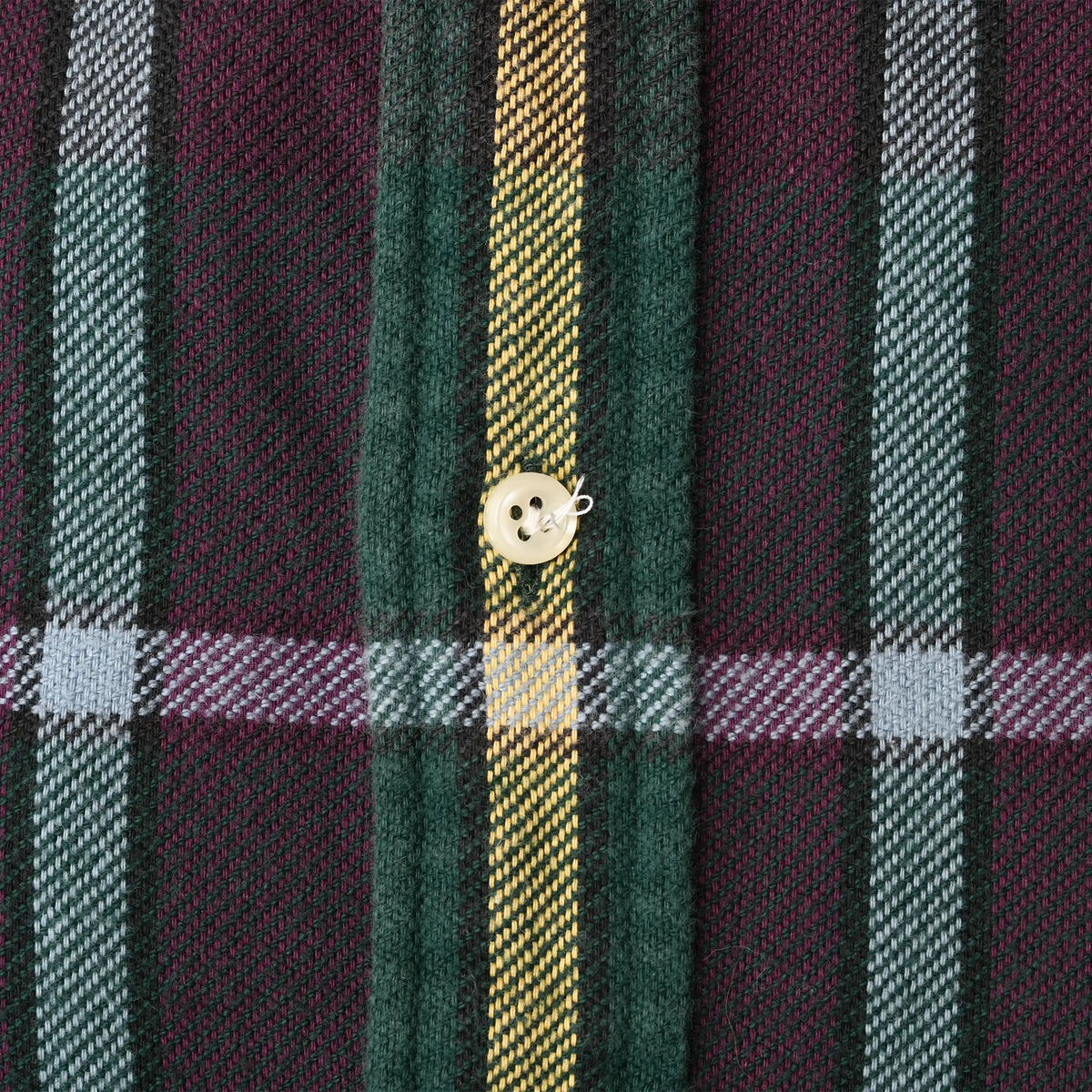 Close-up of cream button with loose thread on green, burgundy, yellow and blue plaid fabric