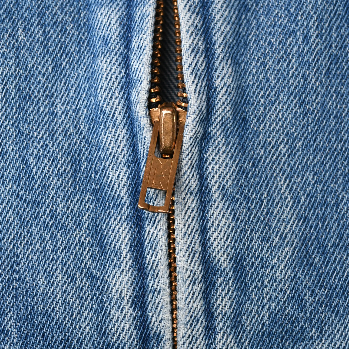 Close-up of metal zipper pull and teeth on blue denim jacket