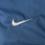 Close-up of white Nike Swoosh embroidery on blue windbreaker fabric