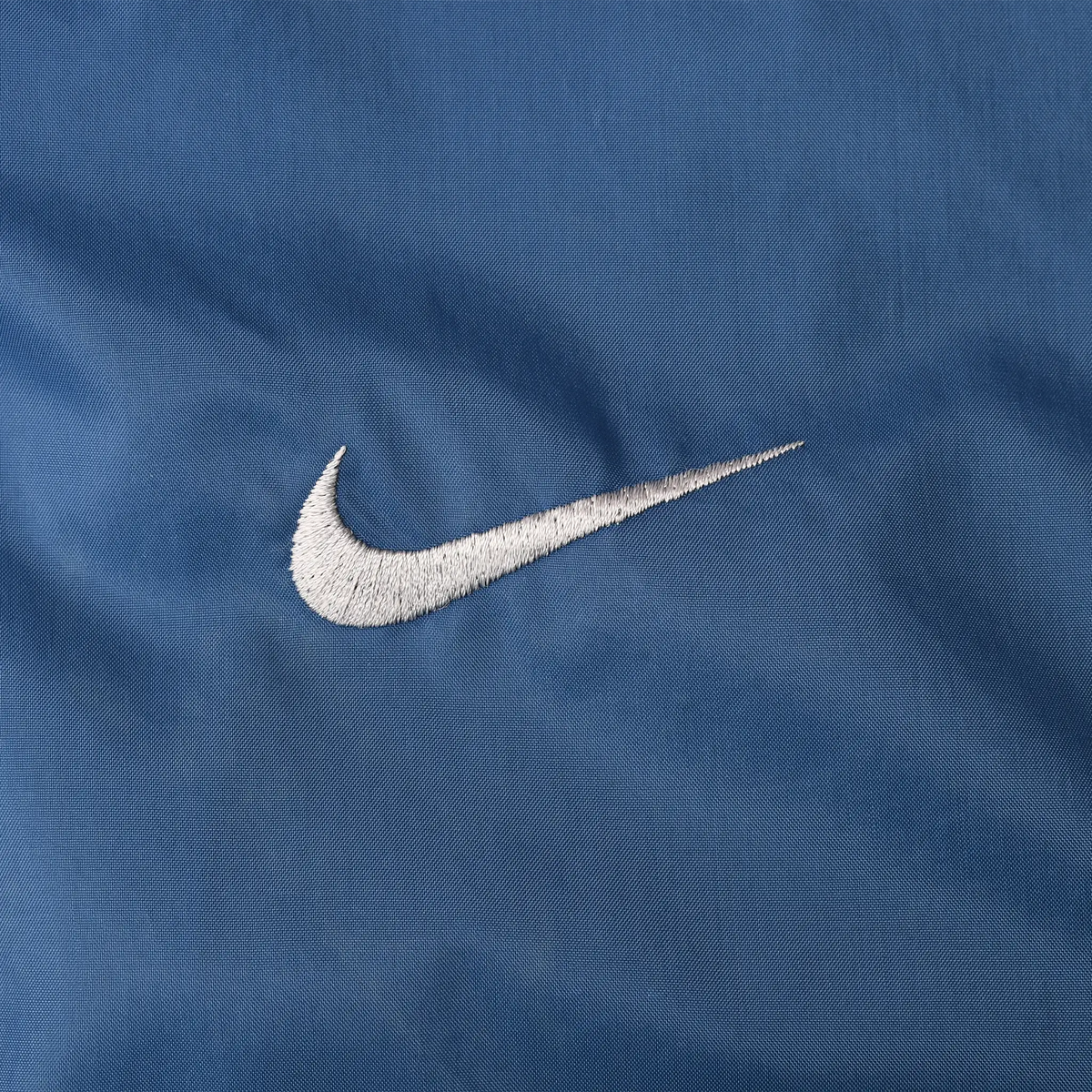 Close-up of white Nike Swoosh embroidery on blue windbreaker fabric