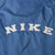 Close-up of white NIKE lettering across the blue windbreaker back