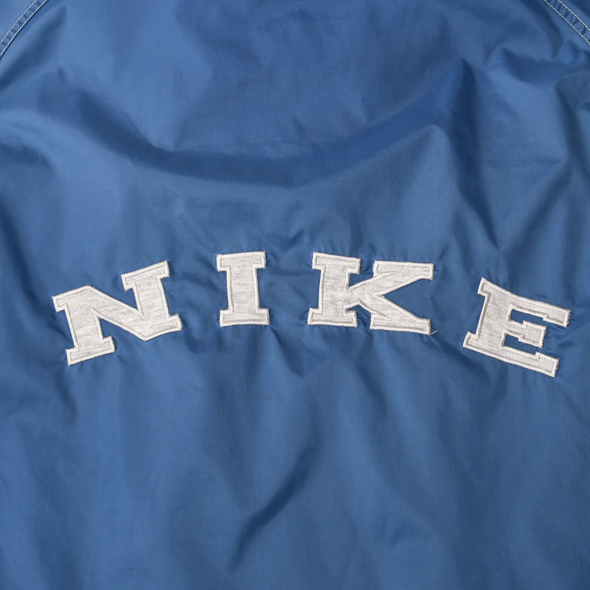 Close-up of white NIKE lettering across the blue windbreaker back