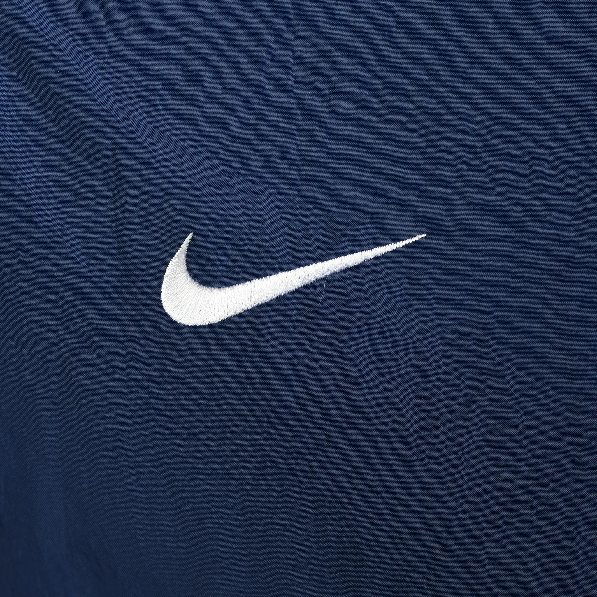Close-up of white embroidered Nike Swoosh on navy windbreaker fabric