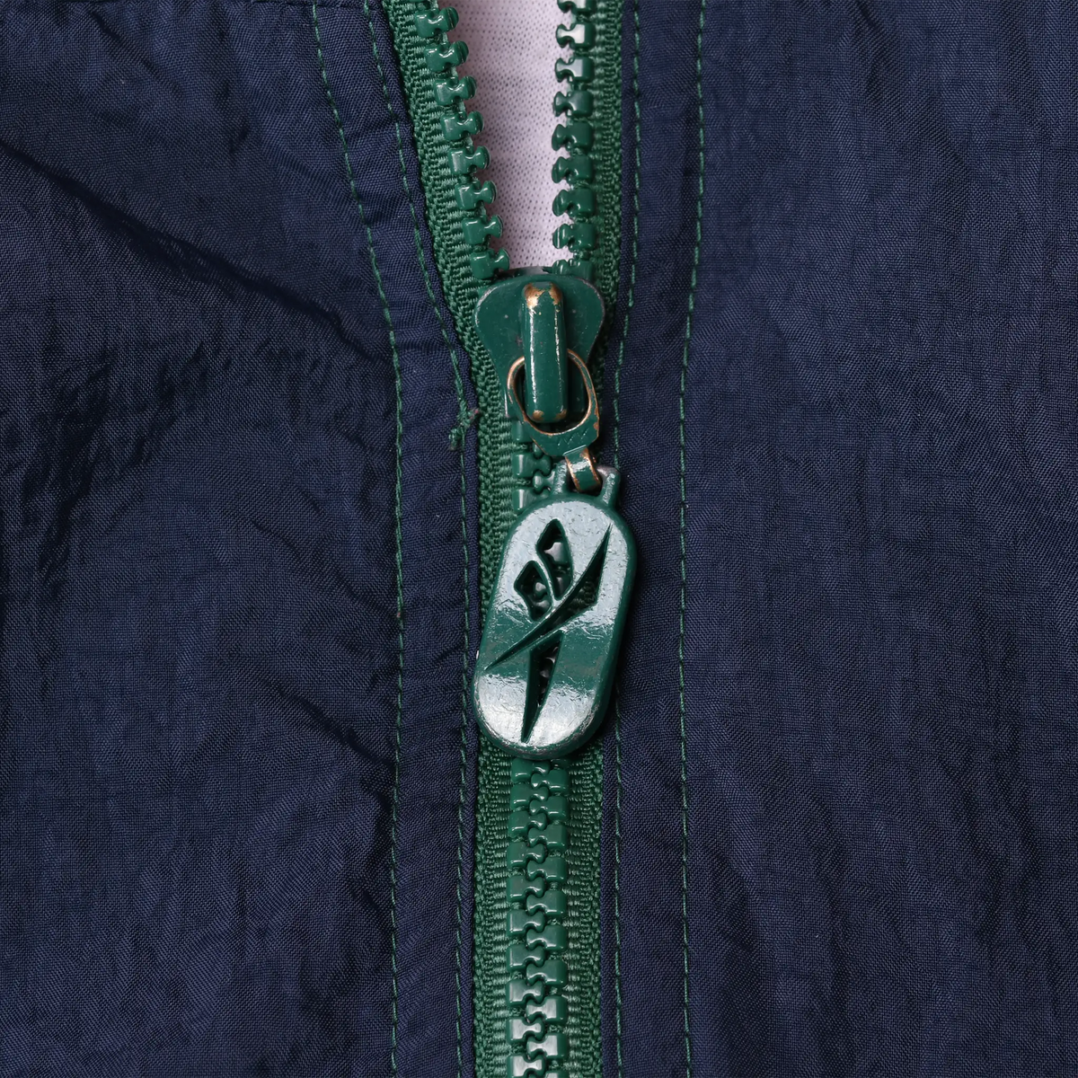 Close-up of green front zipper and Reebok logo zipper pull on navy fabric