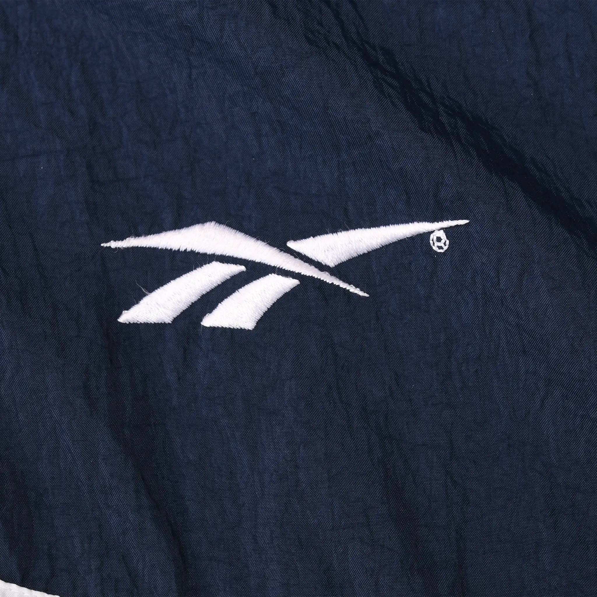 Close-up of small white Reebok logo embroidered on navy jacket chest