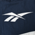 Close-up of large white Reebok logo appliqué on back of navy jacket
