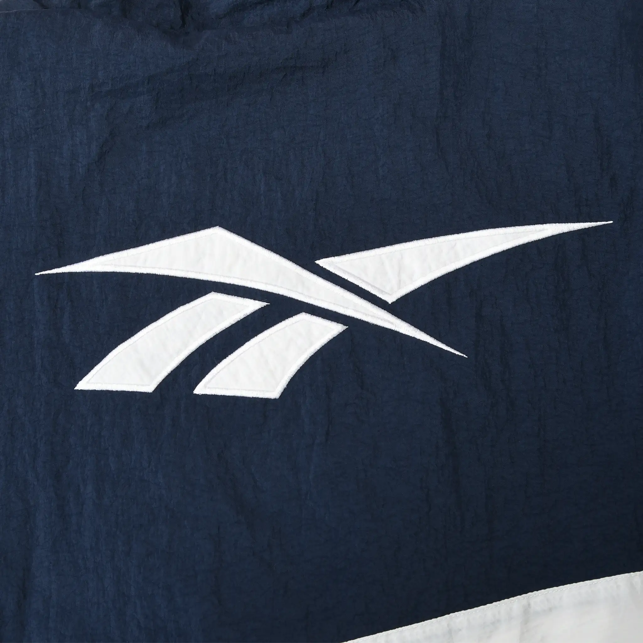 Close-up of large white Reebok logo appliqué on back of navy jacket