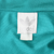 Close-up of white Adidas trefoil neck label against teal fabric