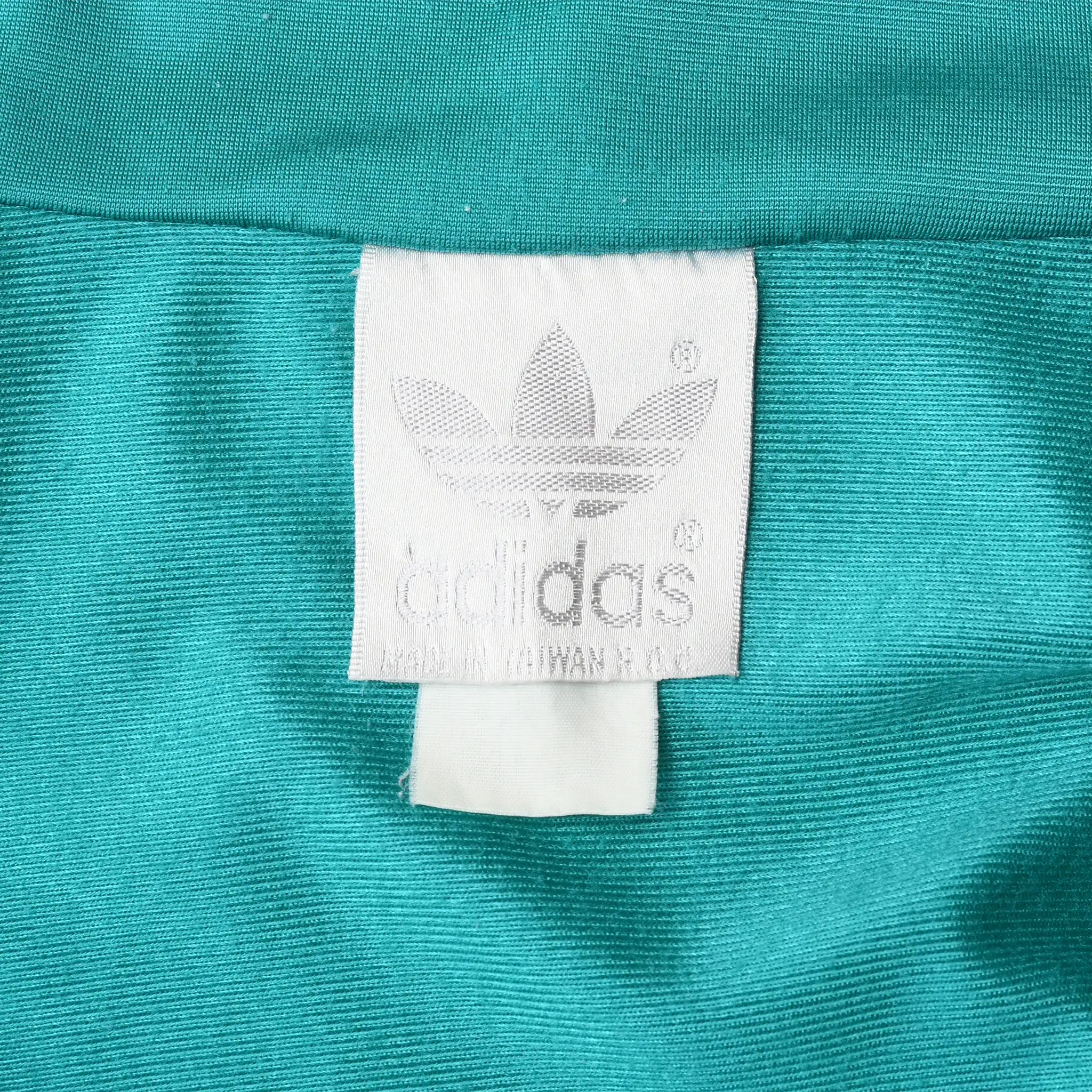 Close-up of white Adidas trefoil neck label against teal fabric