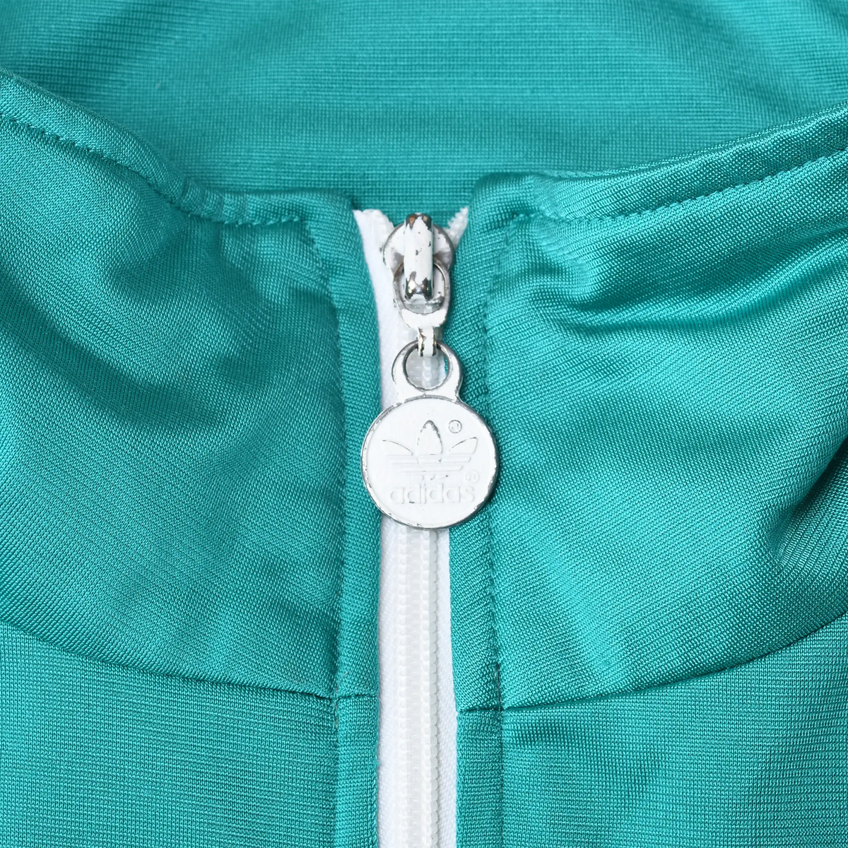 Close-up of silver Adidas trefoil zipper pull and white zipper on teal collar