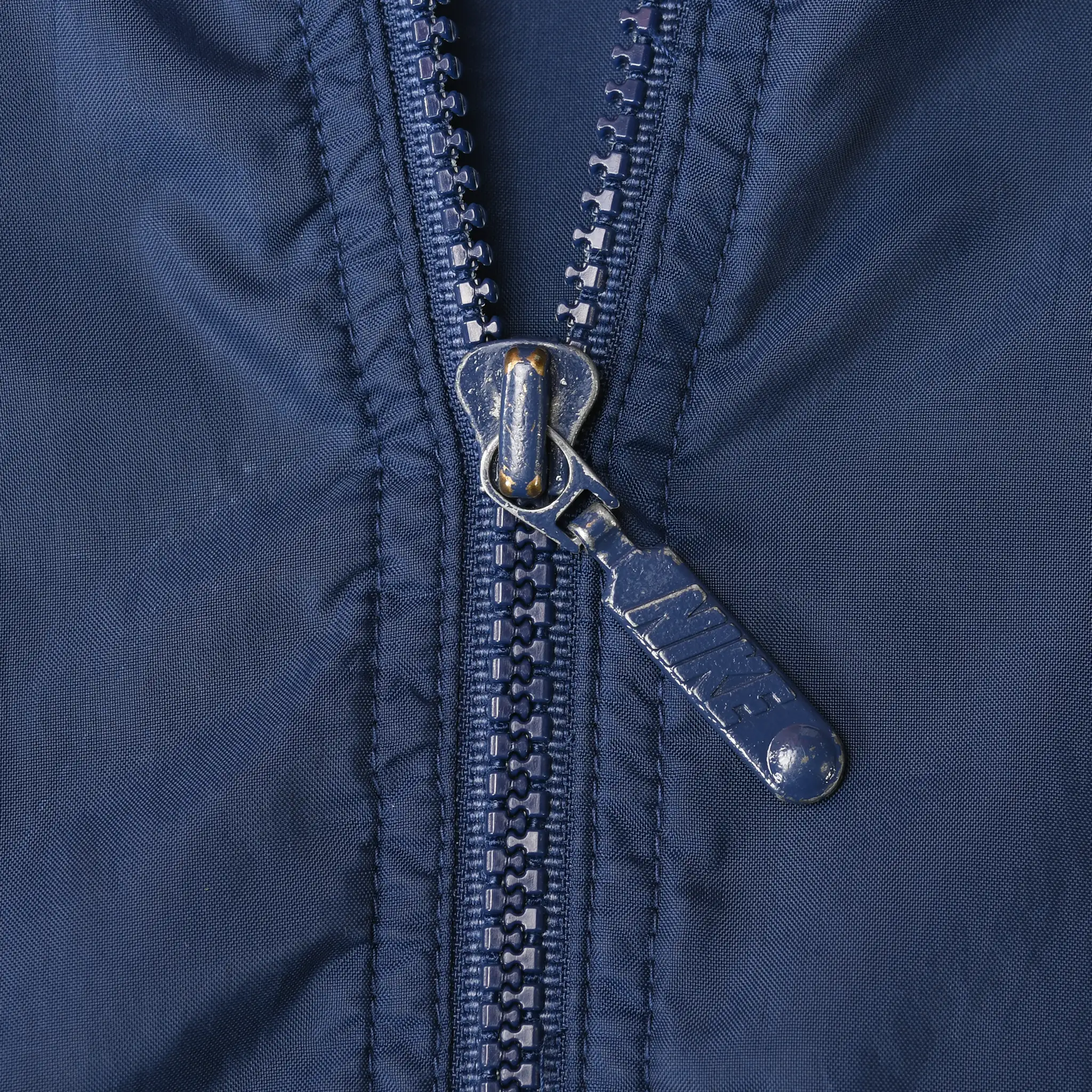 Close-up of the navy windbreaker's front zipper and metal pull