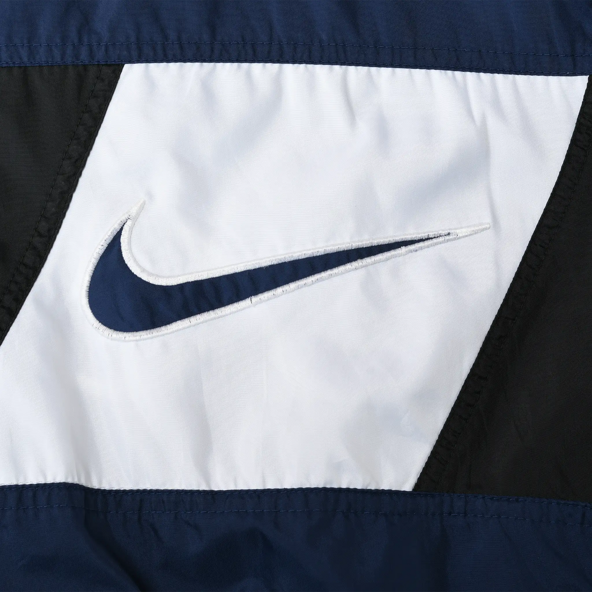 Close-up of navy embroidered Nike Swoosh on the white front chest panel
