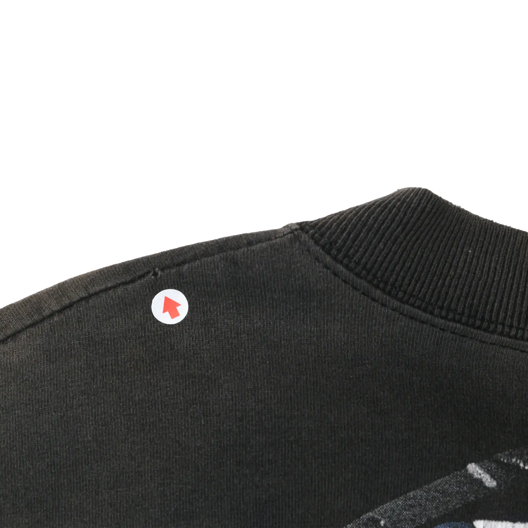 Close-up of black tee shoulder seam and ribbed collar with a small spot marked by an arrow