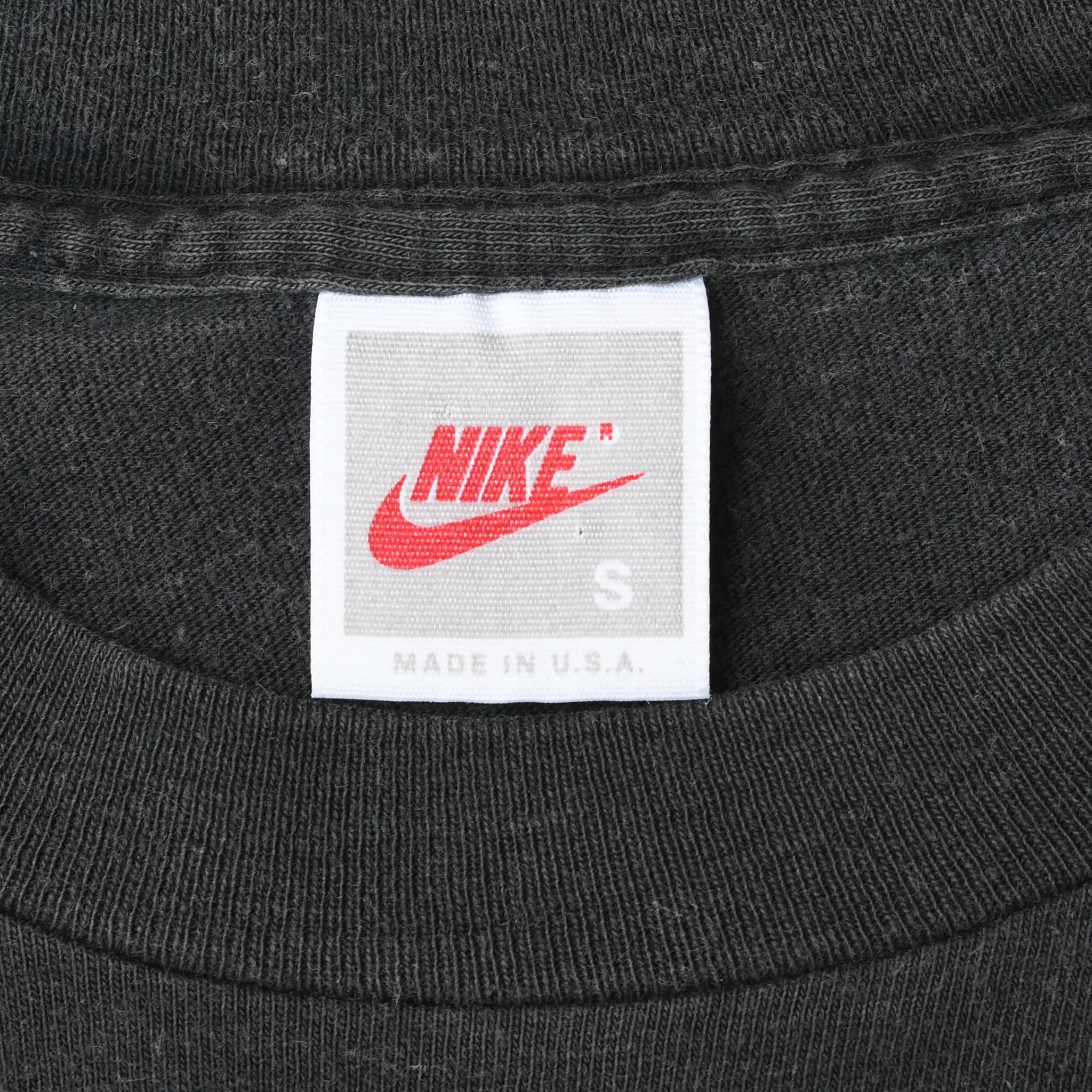 Close-up of white Nike neck tag marked size S and Made in U.S.A. on black fabric