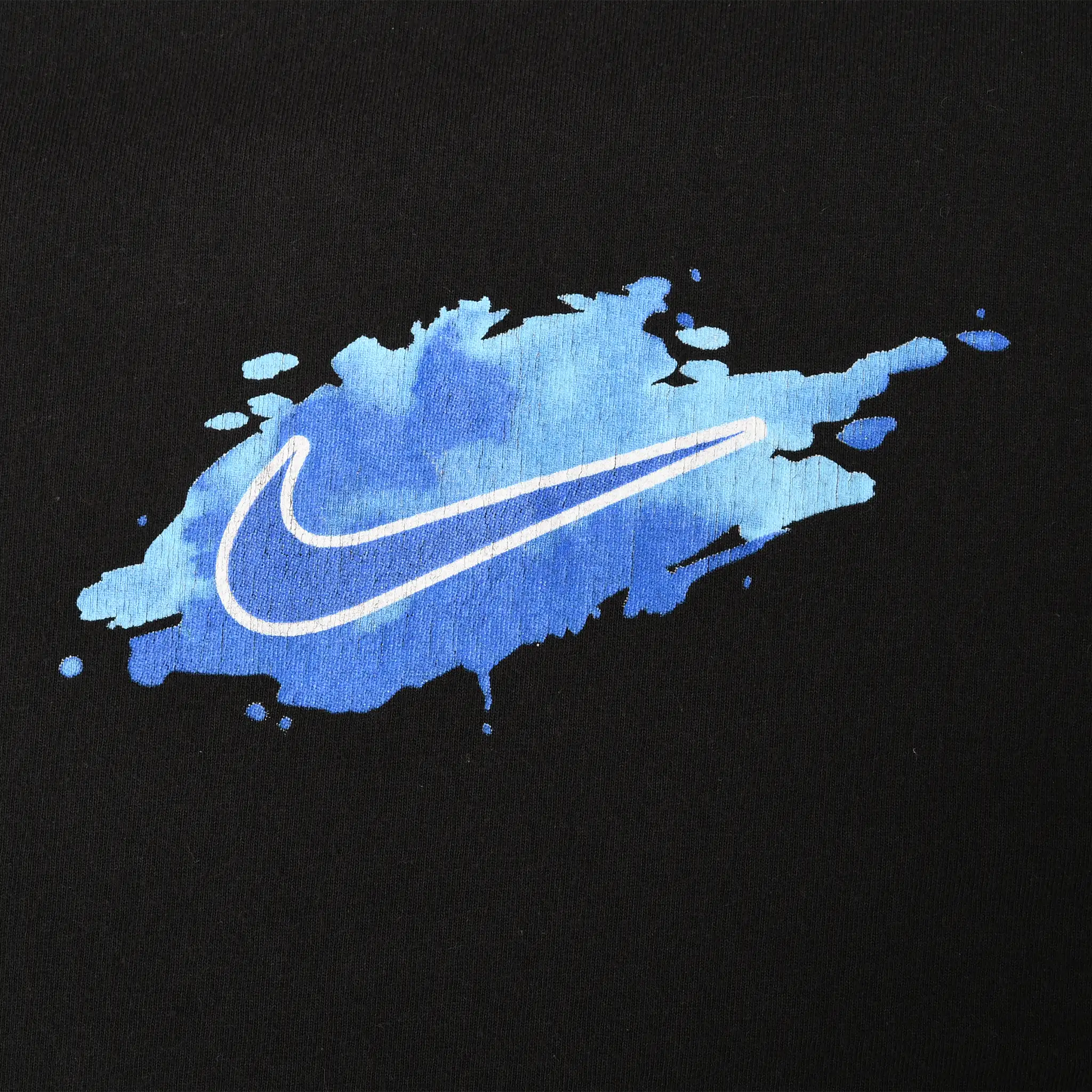 Close-up of blue paint splash graphic with white Nike Swoosh on black fabric