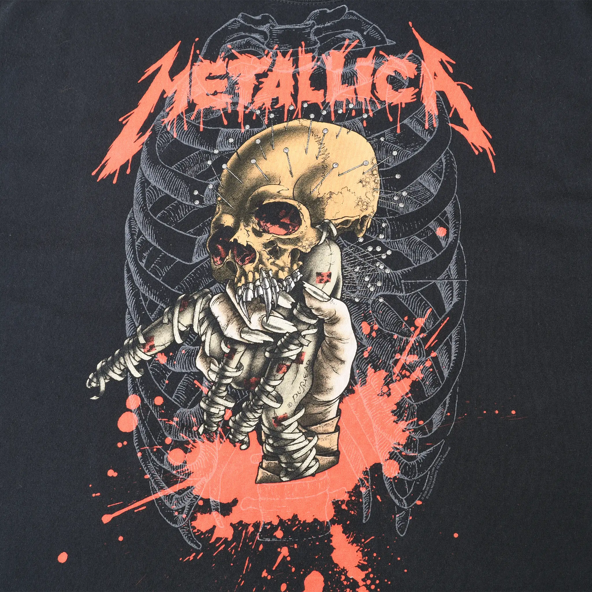 Close-up of Metallica front graphic with red logo, skull, wrapped skeleton, rib cage, and splatter