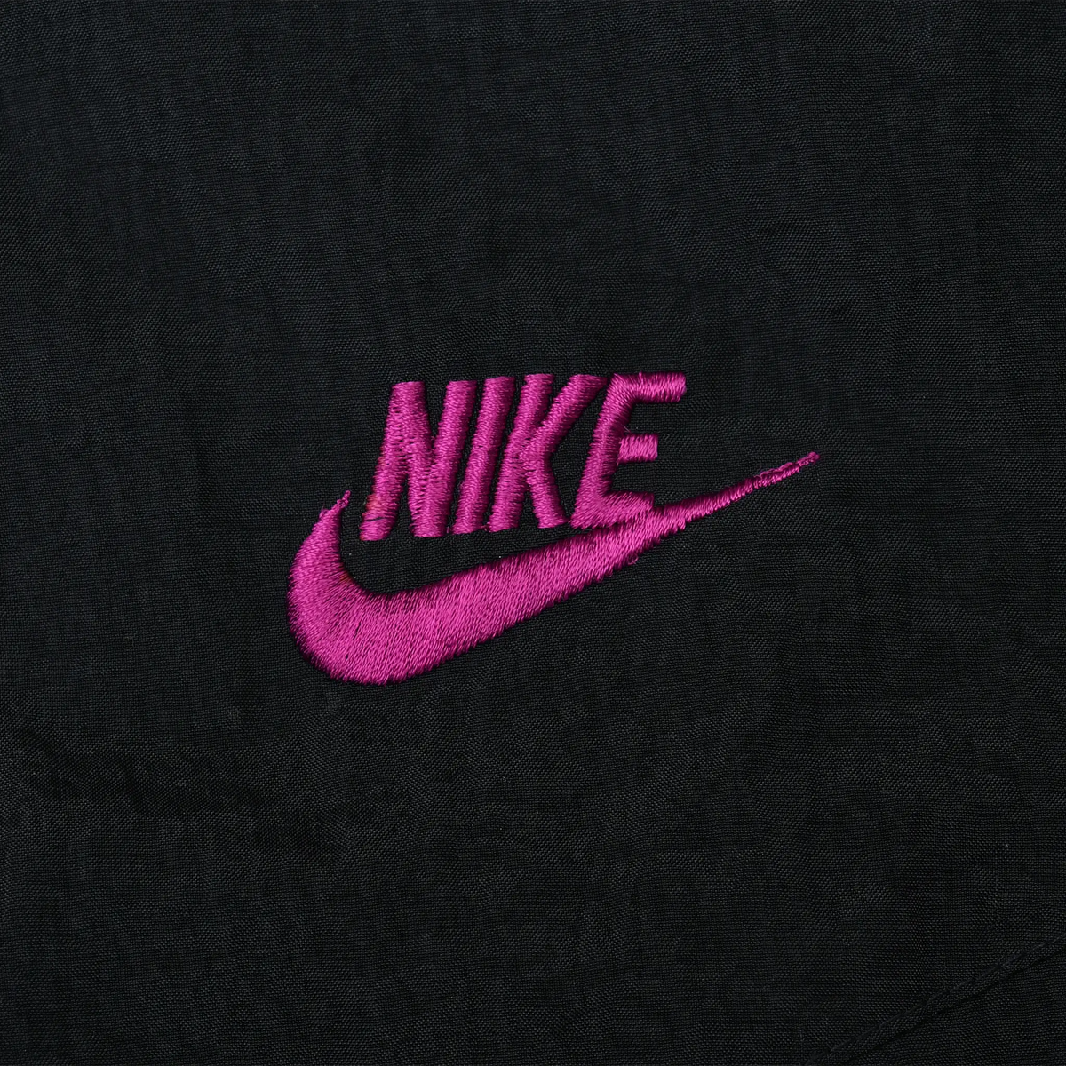 Close-up of purple Nike wordmark and Swoosh embroidery on black chest fabric