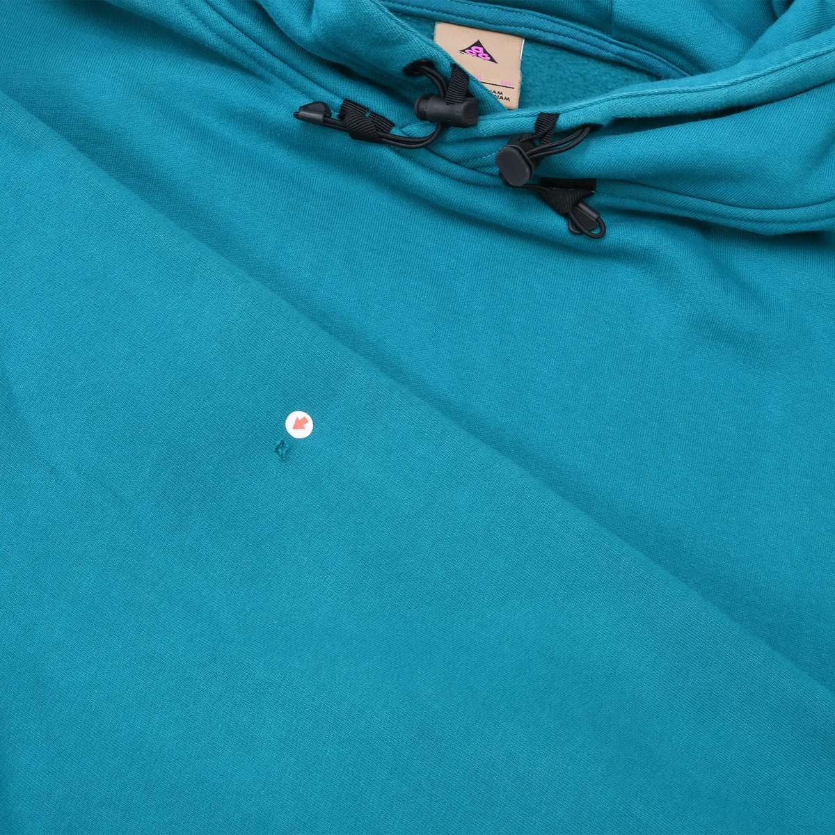 Close-up of teal blue hoodie front showing a small marked spot below the black hood toggles