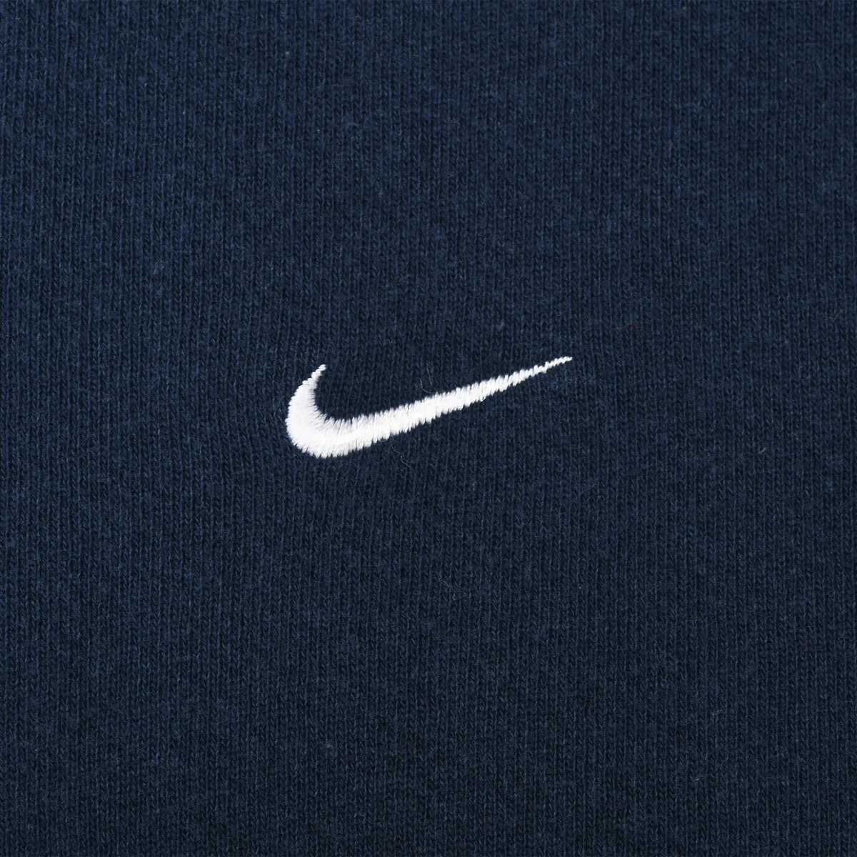 Close-up of small white Nike Swoosh embroidery on navy blue fabric