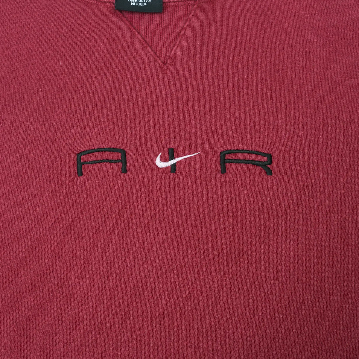 Close-up of black Air lettering and white Nike Swoosh embroidery on burgundy chest