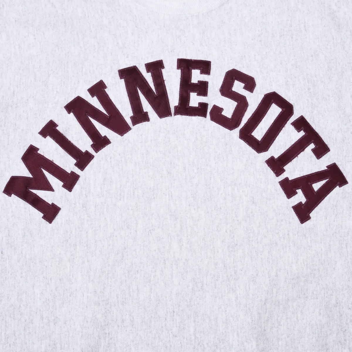 Close-up of arched maroon Minnesota embroidery on gray sweatshirt
