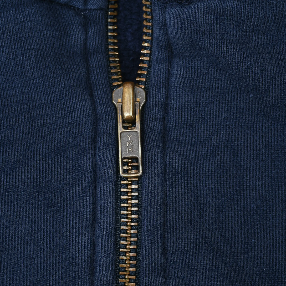 Close-up of brass-tone YKK quarter zipper on navy sweatshirt