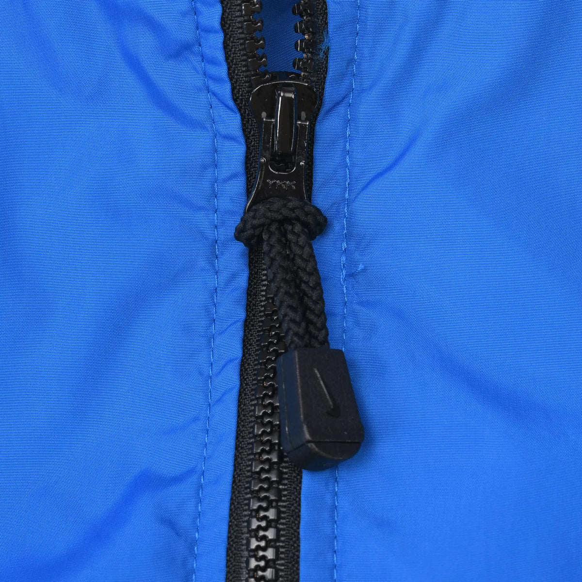 Close-up of black front zipper and corded pull on blue Nike windbreaker jacket