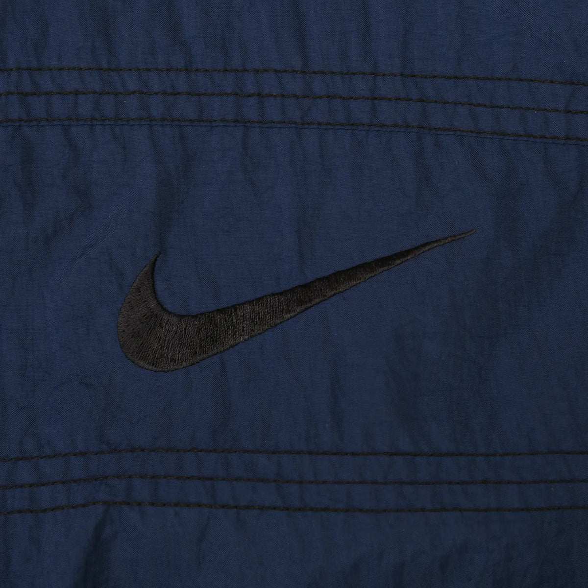 Close-up of black Nike Swoosh embroidery on navy blue jacket chest