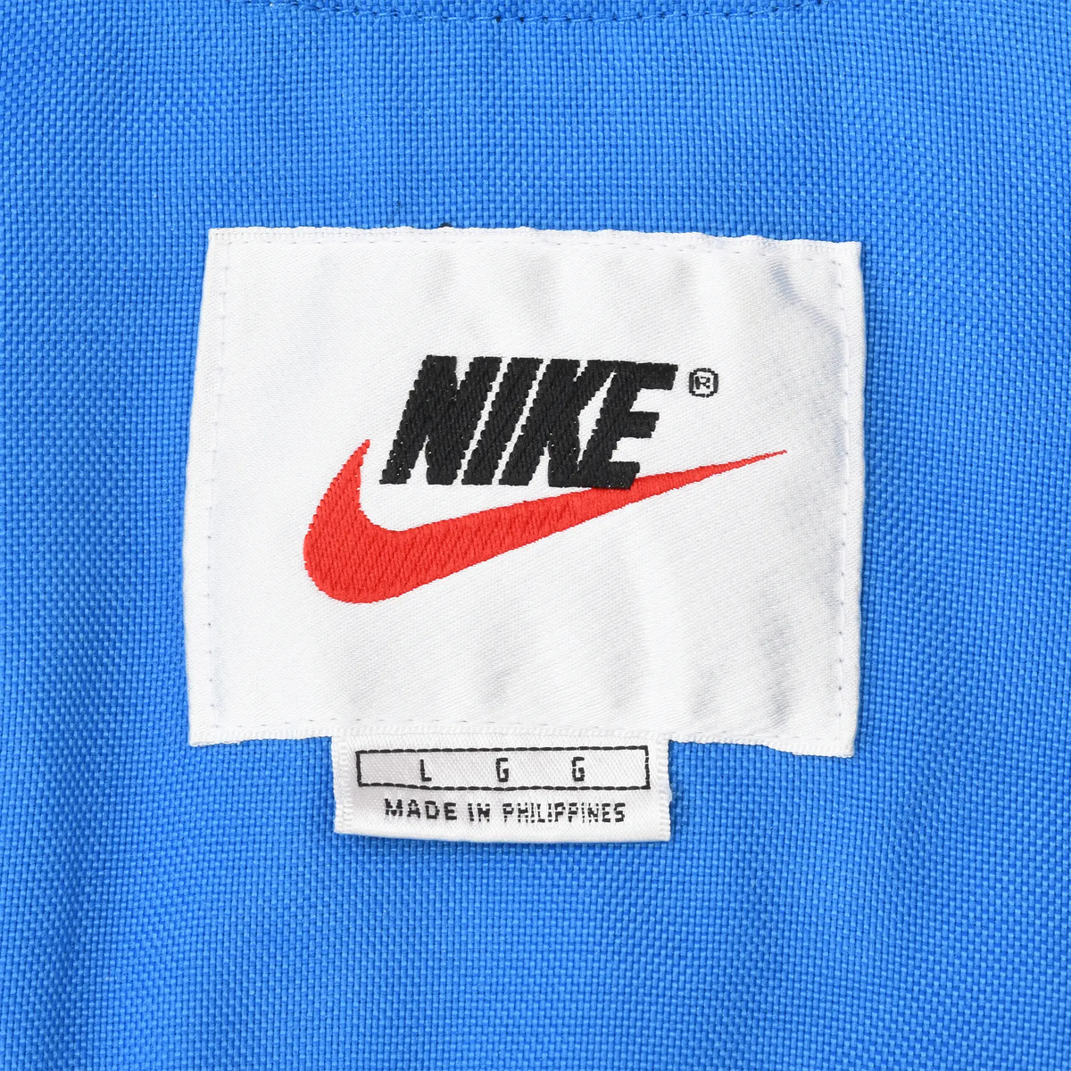 Close-up of white Nike neck label with black logo and red Swoosh on blue fabric