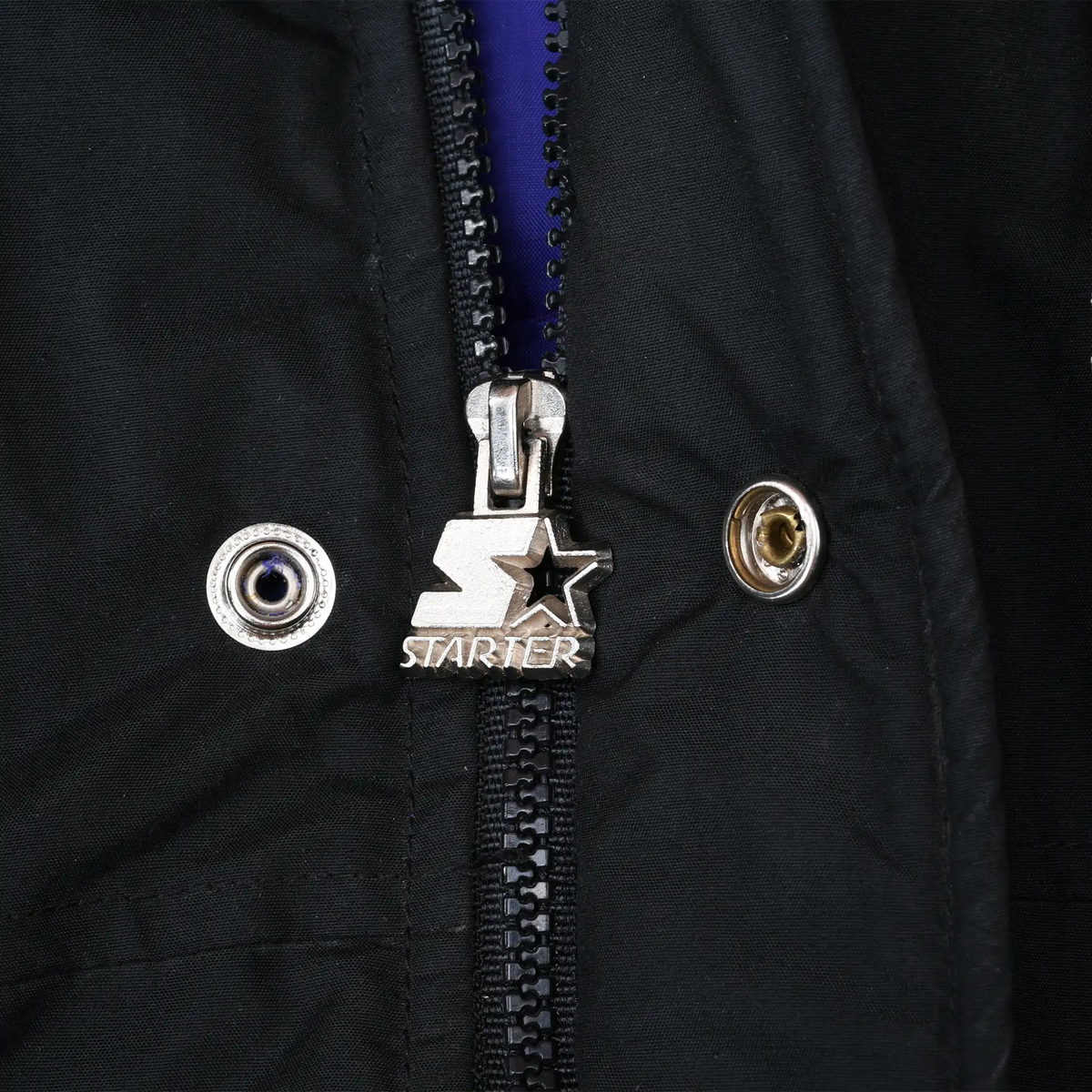 Close-up of silver Starter logo zipper pull and snap closures on black jacket