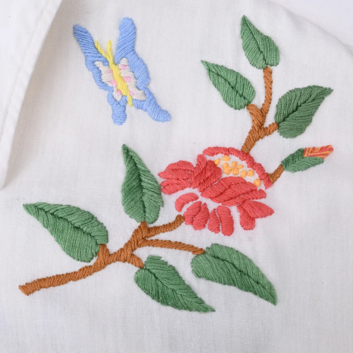 Close-up of red flower, green leaves, and blue butterfly embroidery on white fabric